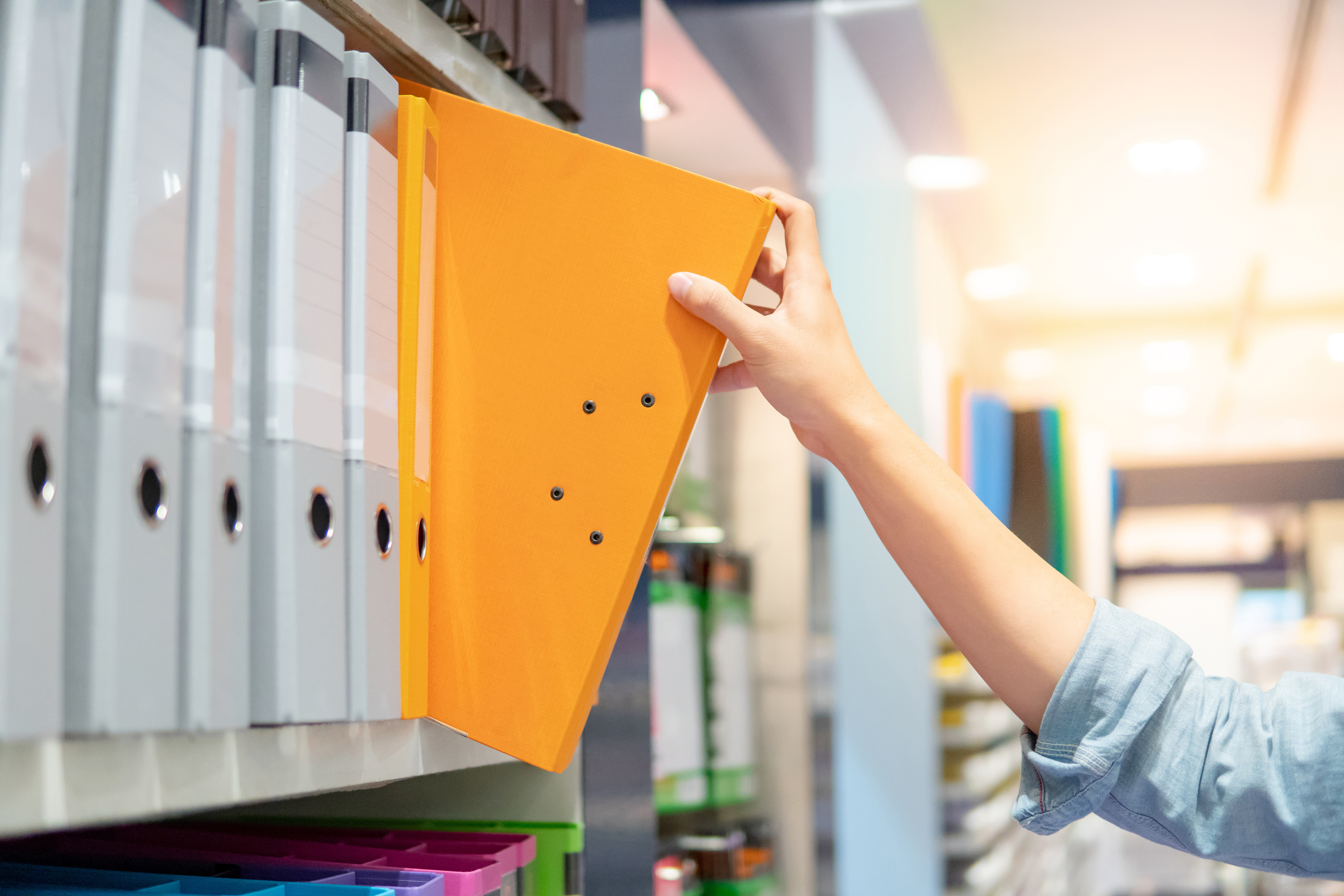 a person pulling out an orange binder on the shelves