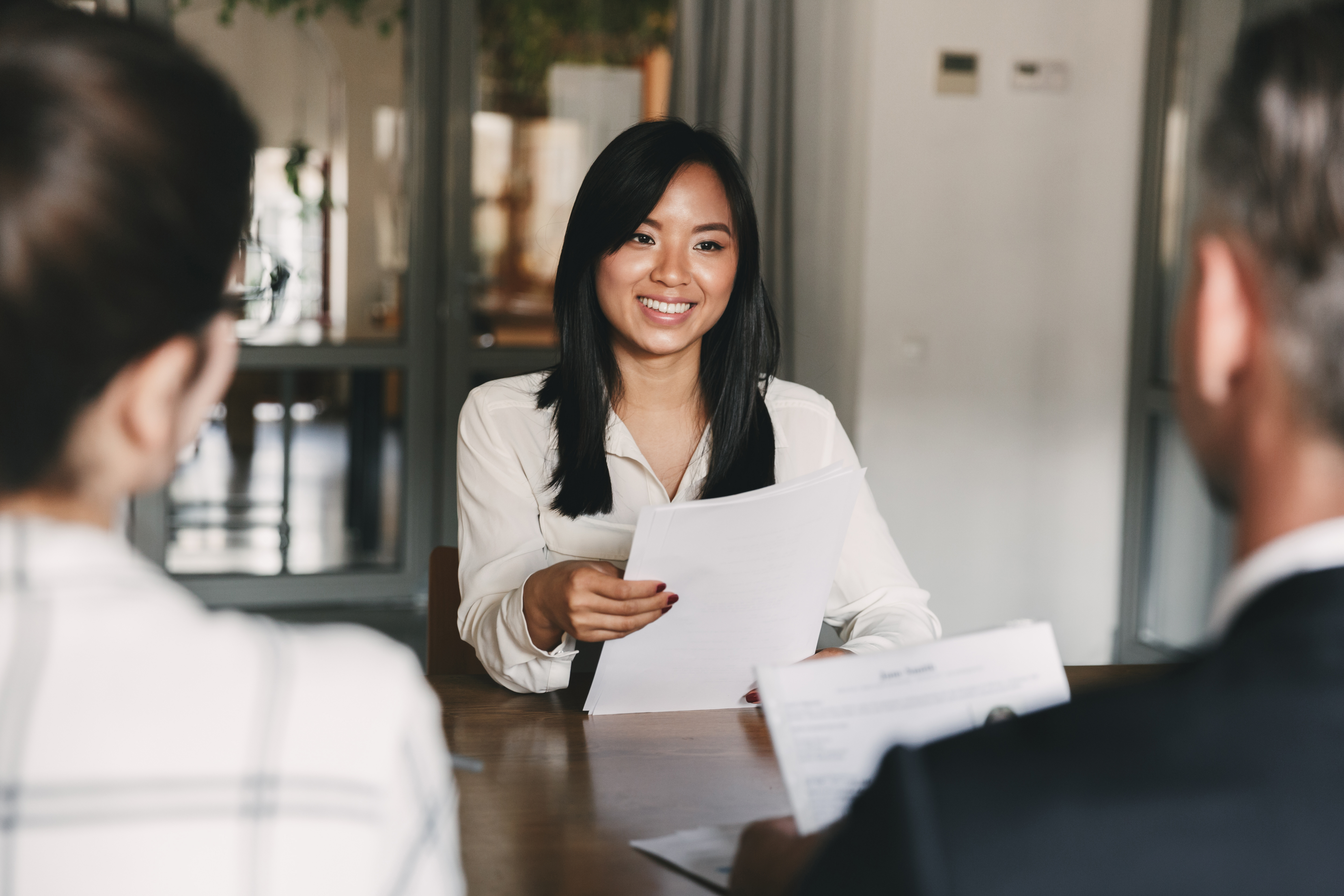 a young lady sitting opposite of 2 people holding a piece of paper and smiling