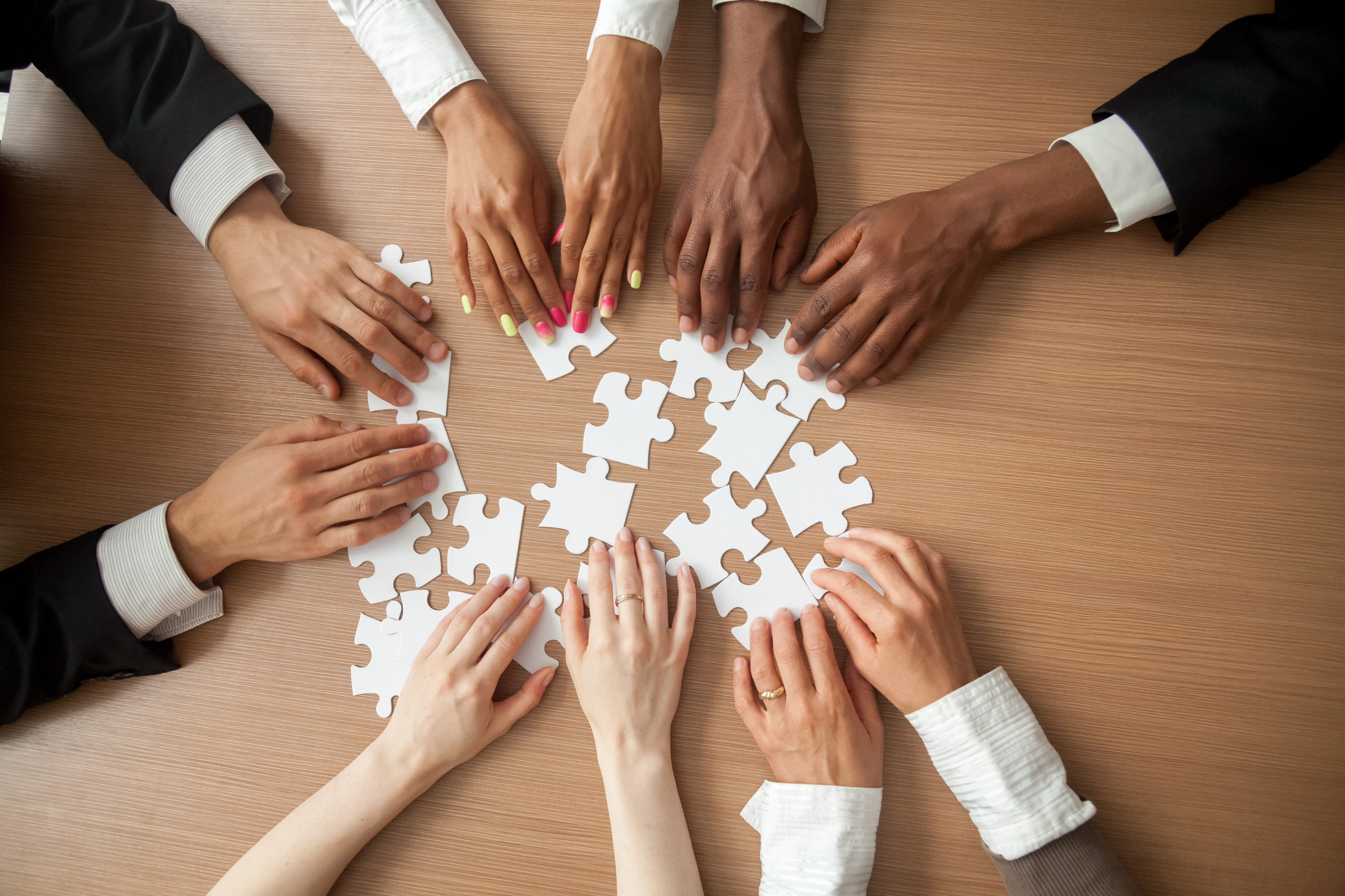 5 pairs of hands touching many puzzle pieces on the table