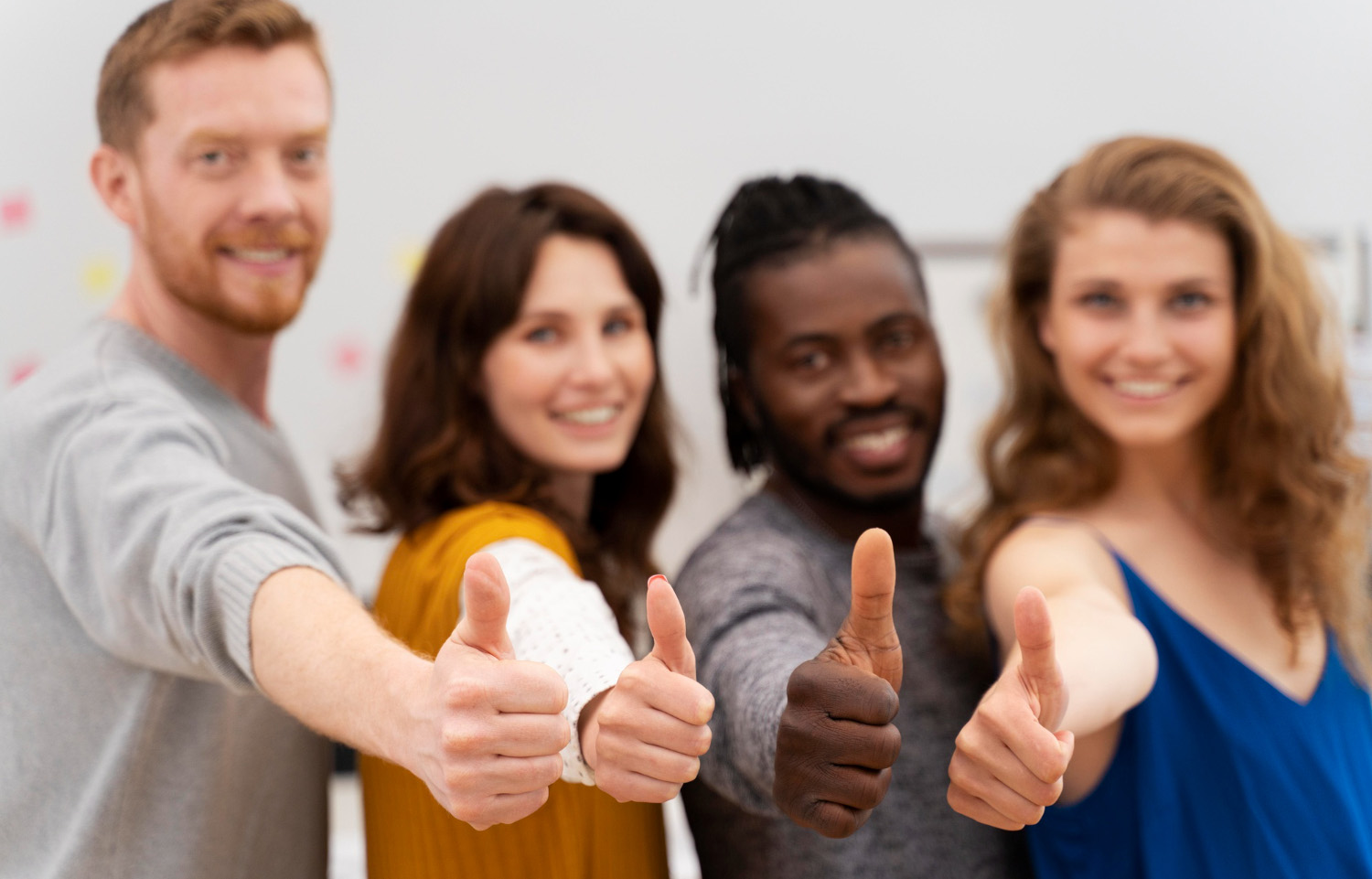 Four people standing shoulder to shoulder all giving "thumbs up"